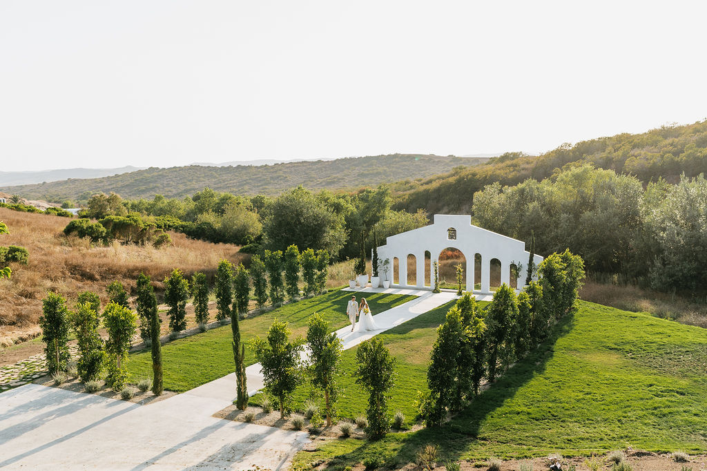 Jeune Perche Estate wedding ceremony space, bride and groom walking down aisle in front of arch backdrop, rolling hills.