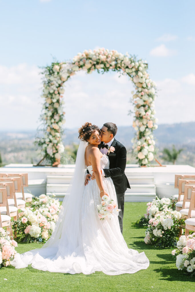 Bride and groom sharing a kiss in the aisle surrounded by florals at The Hillside Estate.