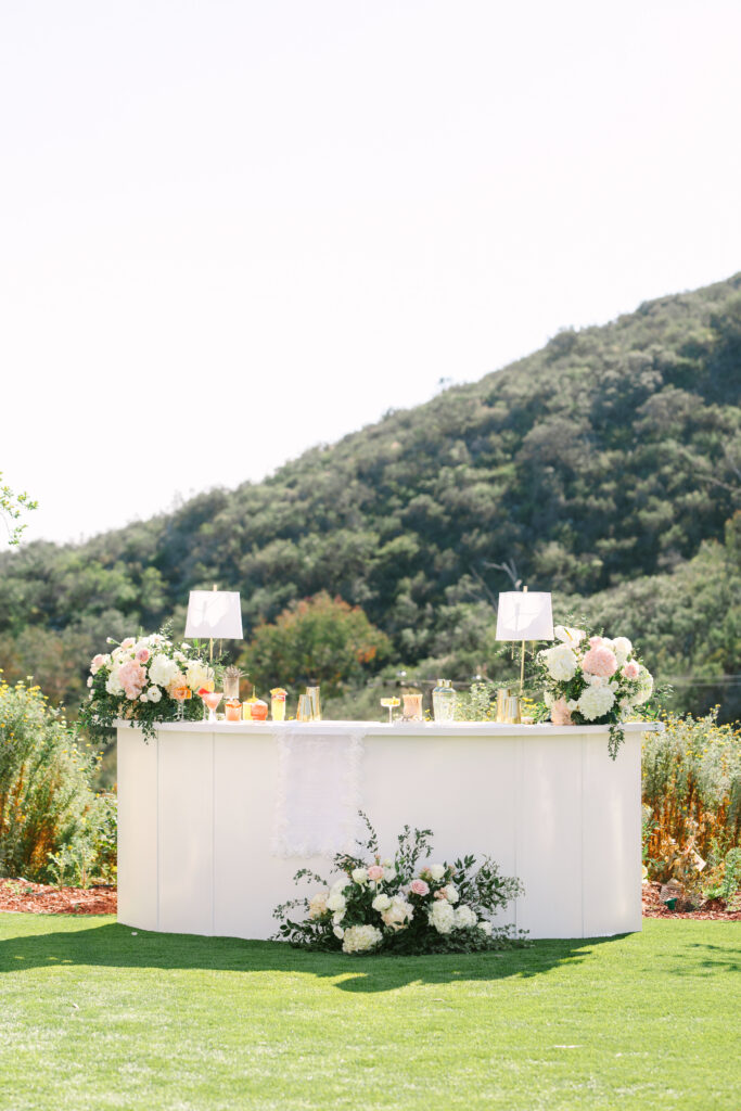 Floral-decorated white cocktail hour bar with signature drinks in front of vineyard views at The Hillside Estate.