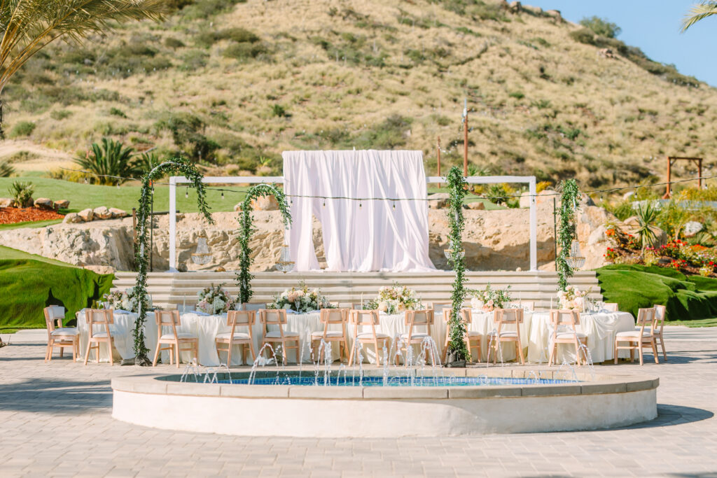 Outdoor wedding reception courtyard with fountain, draped backdrop, floral-wrapped columns, and hillside views at The Hillside Estate private estate wedding venue in San Marcos, California.