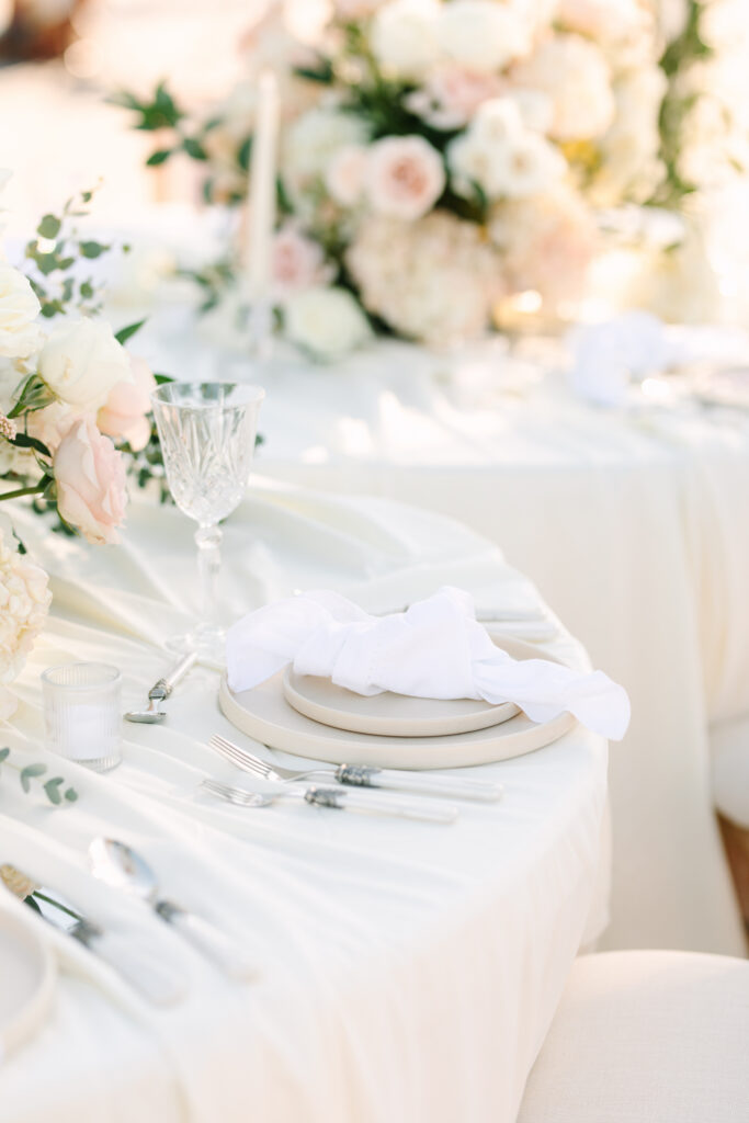 Close up of wedding reception place setting with neutral plates, white linen napkin, crystal glassware, and blush floral centerpiece at The Hillside Estate.