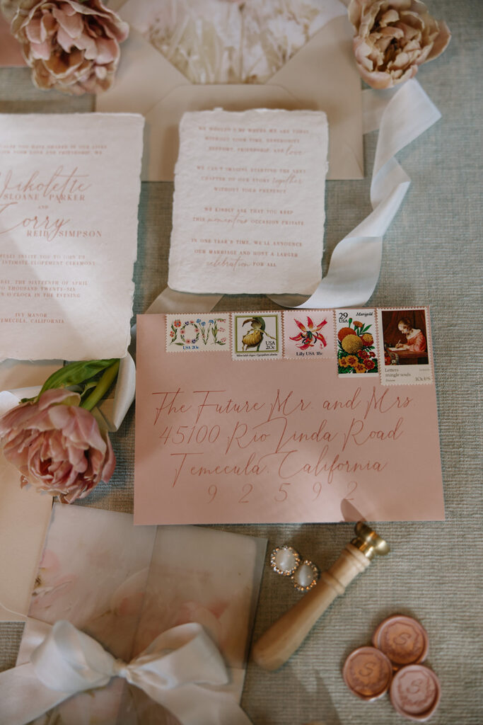 Blush wedding envelope with calligraphy addressing, vintage postage stamps, and wax seals designed by Beach City Creative for an elopement at Ivy Manor Temecula.