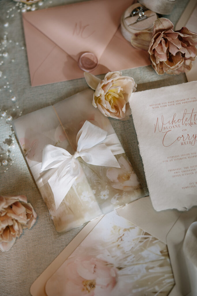 Close up of a vellum wrapped wedding invitation with silk ribbon bow and blush floral details designed by Beach City Creative for a Temecula elopement.
