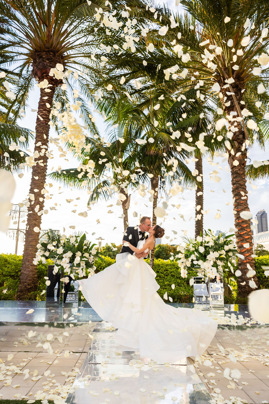Bride and groom share their first kiss as white rose petals fill the air at their Hilton San Diego Bayfront Wedding