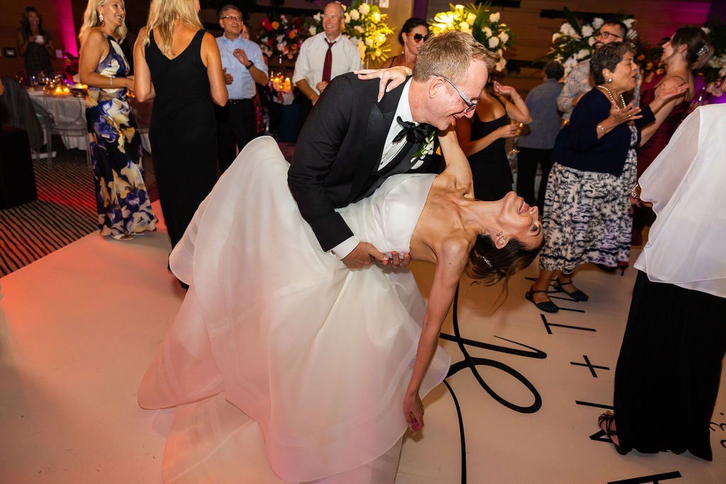 Groom dips bride on the custom monogram dance floor during the reception at a Hilton San Diego Bayfront Wedding, surrounded by guests and vibrant uplighting