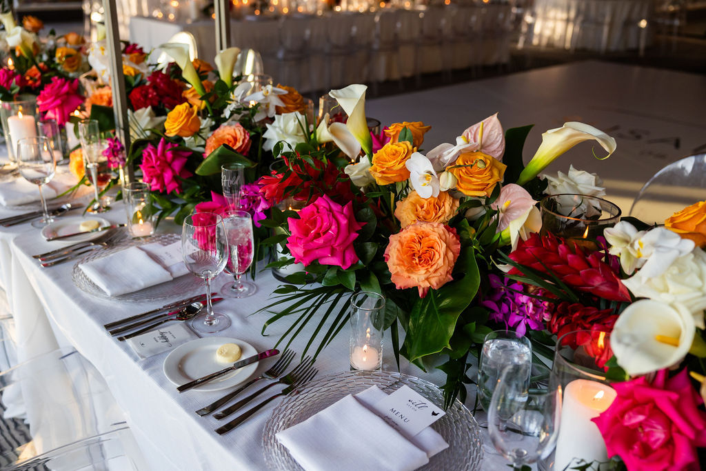 Tropical reception tablescape at a Hilton San Diego Bayfront wedding featuring vibrant pink, orange, and peach florals with palm leaves running the length of the head table