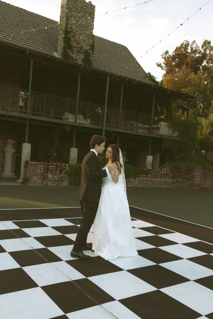 Bride and groom dancing on the chessboard dance floor at Ivy Manor Temecula with the ballroom building in the background.