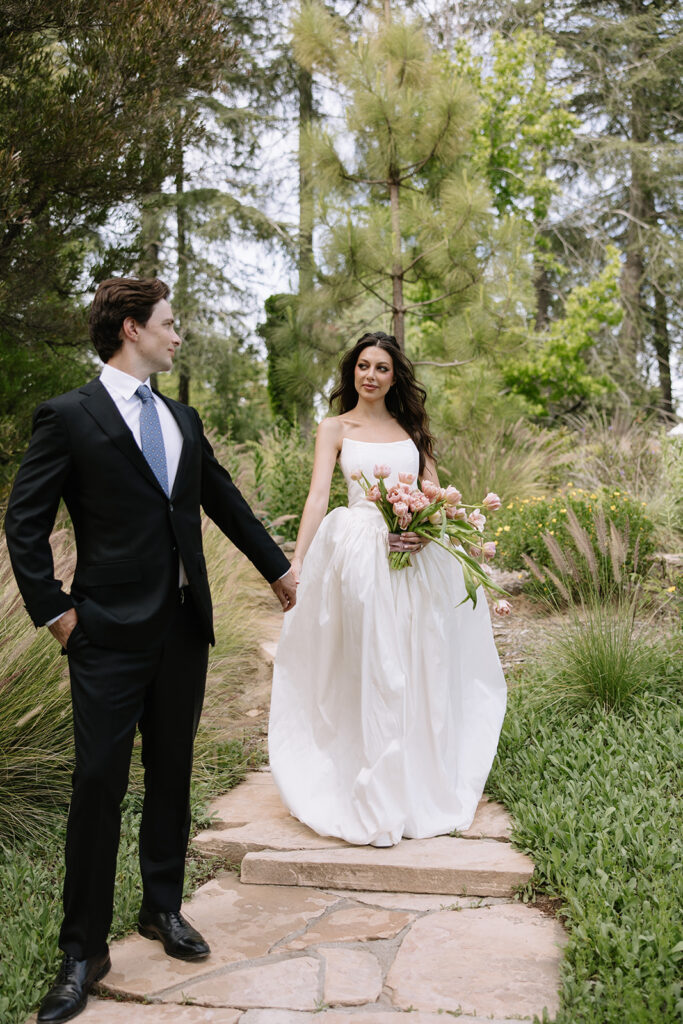 Bride and groom walking hand in hand along a stone garden path at Ivy Manor Temecula.