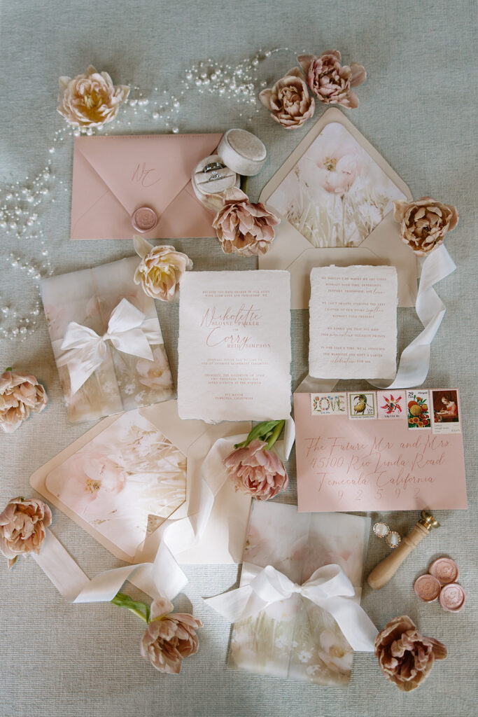 Soft floral wedding invitation suite with vellum wraps, silk ribbon, blush envelopes, handmade paper, and calligraphy addressing with vintage postage designed by Beach City Creative for an elopement at Ivy Manor Temecula.